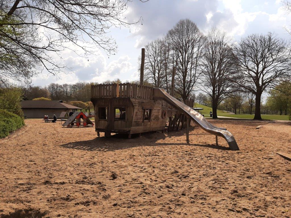 Das Bild zeigt ein großes Schiff auf Holz, das umgeben von Sand als Spielmöglichkeit für Kinder dient.