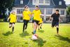 Sechs Kinder und Jugendliche mit und ohne Behinderung spielen auf einer Wiese Fußball.