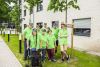Eine Gruppe von neun Personen stehen vor einem Haus. Sie sind unterschiedlich alt. Alle tragen grüne T-Shirts.
